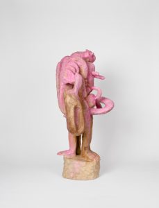 Hand-carved wooden sculpture composed of intertwined anthropomorphic forms arranged within a vertical composition. Multiple heads and elongated limbs are connected by carved wooden elements and integrated metal components. The surface is finished with stain, ink, varnish, and wax, revealing the wood grain beneath the carved surface.