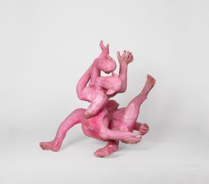 Hand-carved wooden sculpture composed of intertwined anthropomorphic forms with multiple heads and projecting limbs arranged in a compact vertical composition. The surface is finished with stain, ink, varnish, and wax, allowing the wood grain and carved tool marks to remain visible
