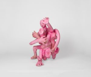 Hand-carved wooden sculpture composed of interconnected anthropomorphic figures with intertwined limbs and multiple heads. The compact composition is finished with stain, ink, varnish, and wax, revealing the wood grain beneath carved surfaces and visible tool marks.