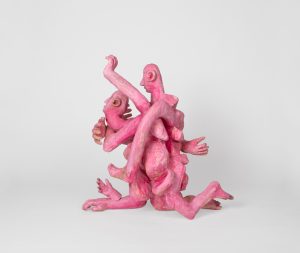 Hand-carved wooden sculpture composed of interconnected anthropomorphic figures with intertwined limbs and multiple heads. The compact composition is finished with stain, ink, varnish, and wax, revealing the wood grain beneath carved surfaces and visible tool marks.